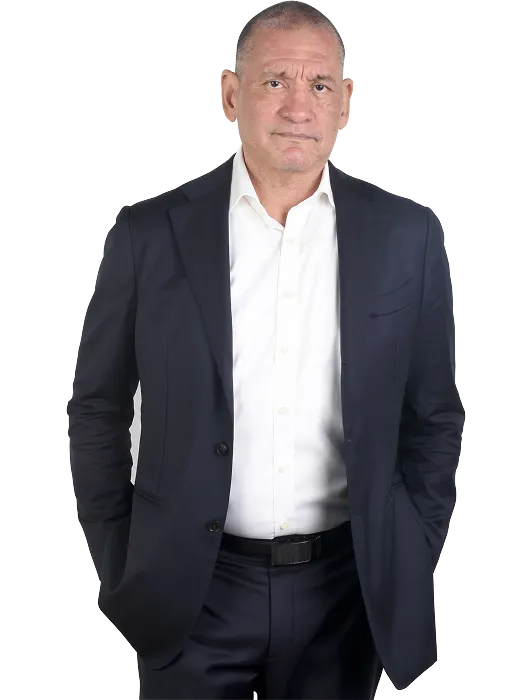 Middle-aged man with short hair wearing a dark suit and white shirt, hands in pockets.