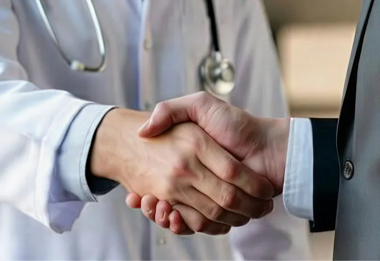 Close-up of a handshake between a doctor in white coat and a person in a dark suit.