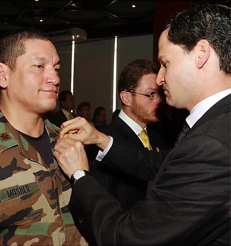 A man in a suit pins a medal on a uniformed soldier named Mosher in an indoor formal setting.
