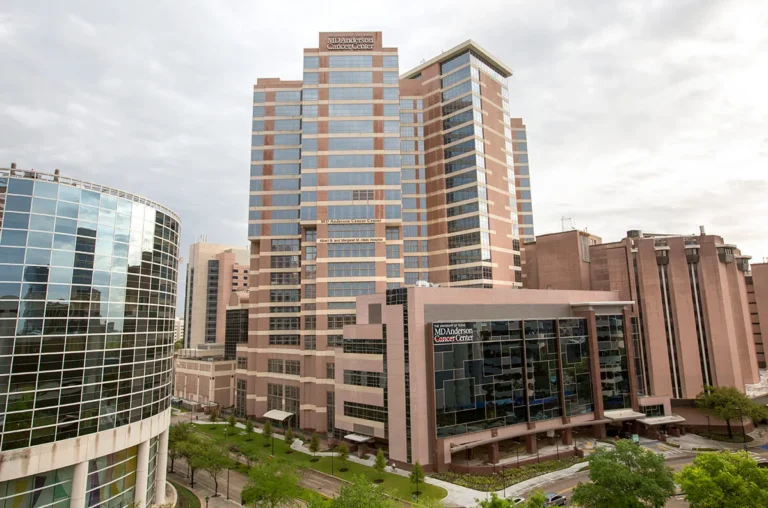 Exterior view of MD Anderson Cancer Center buildings with glass and brick facades under a cloudy sky.