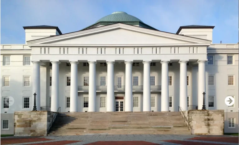 Front view of a large white neoclassical building with tall columns and a green dome.