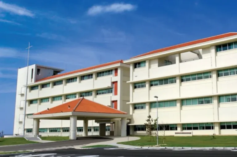 Modern four-story institutional building with white walls, red-tiled roof, and clear blue sky background.