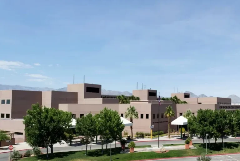 Modern beige institutional building surrounded by green trees and clear blue sky.