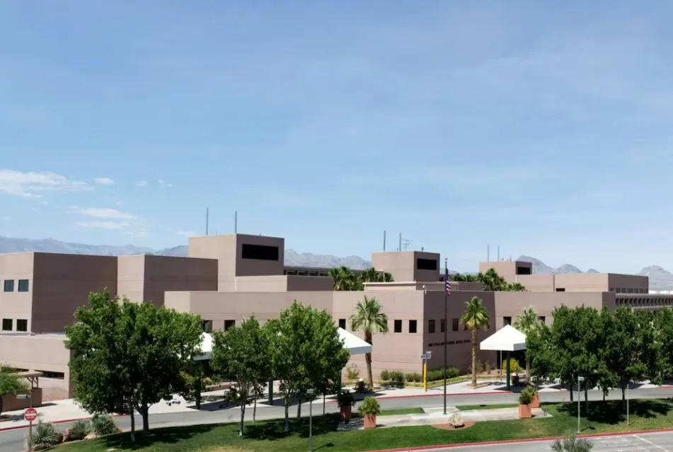 Modern beige institutional building surrounded by green trees and clear blue sky.