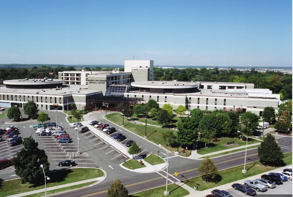 Aerial view of Wright-Patterson Medical Center surrounded by parking lots, trees, and roads under a clear blue sky.