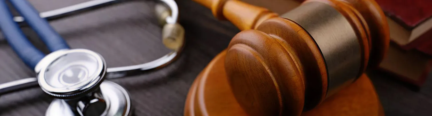 Close-up of a wooden judge's gavel, stethoscope, and law books on a dark surface.