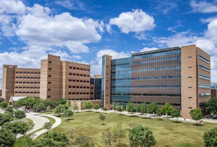Modern institutional buildings with glass and brick facades under a partly cloudy blue sky.