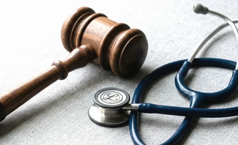 Wooden judge's gavel and blue stethoscope placed on a light gray fabric surface.