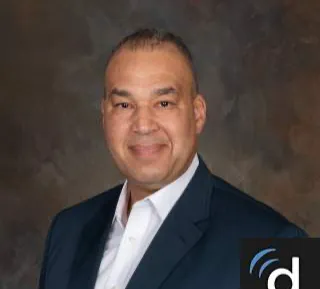Professional headshot of a man in a dark suit jacket and white shirt against a neutral background.