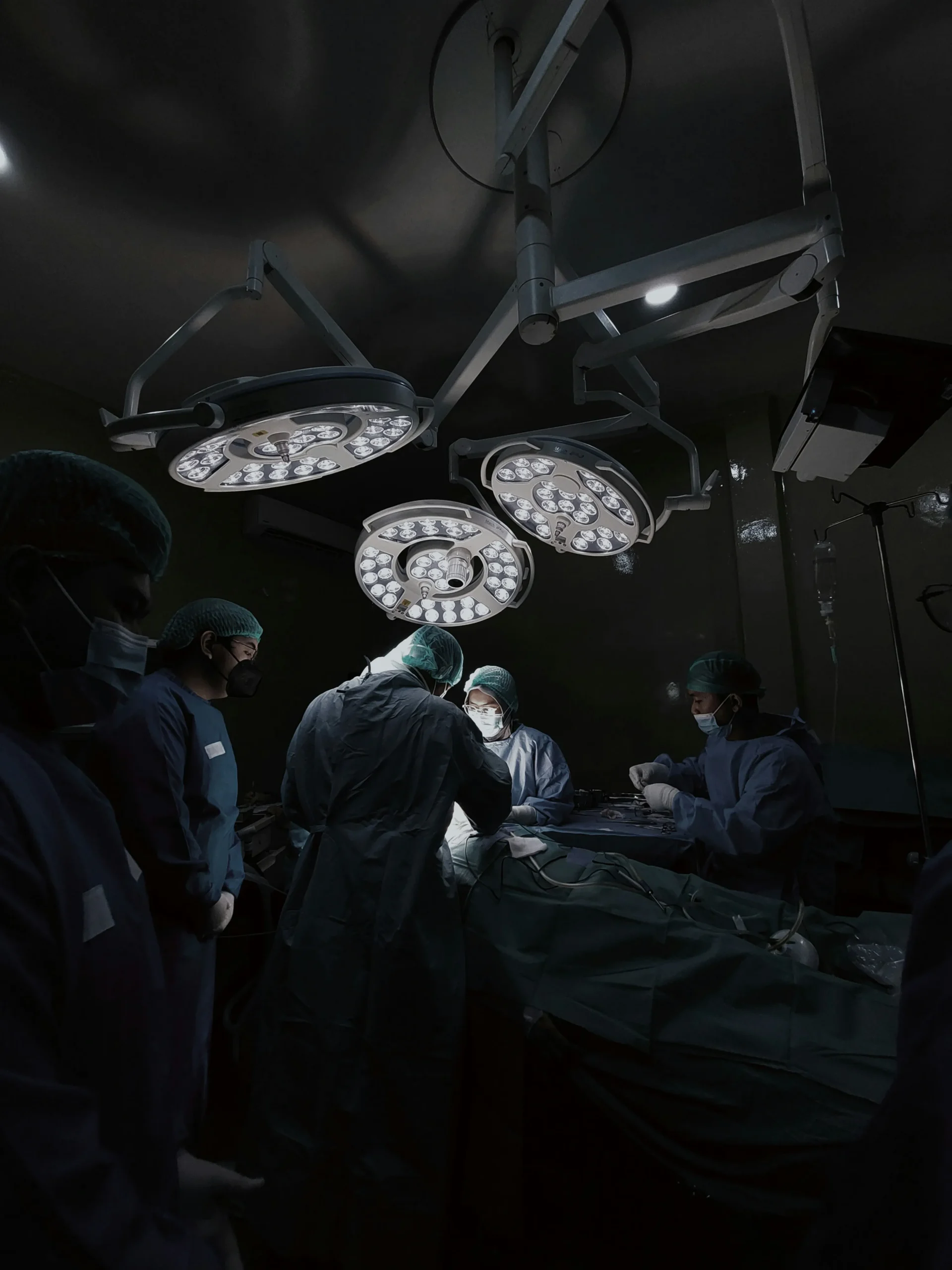 Surgical team in blue scrubs and masks performing operation under bright ceiling lights.