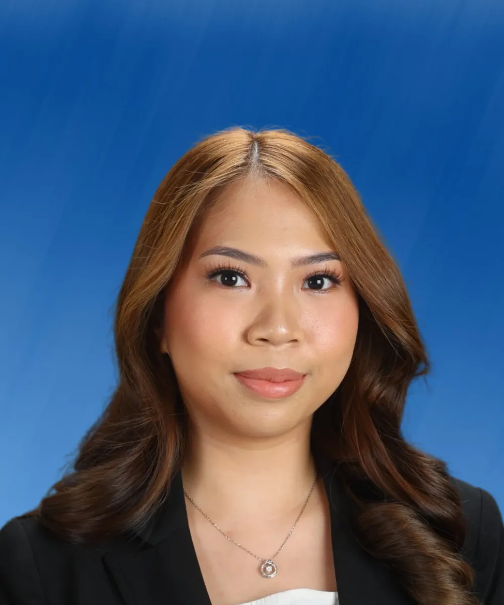 Professional headshot of a woman with light brown hair, wearing a black blazer and silver necklace, against a blue background.