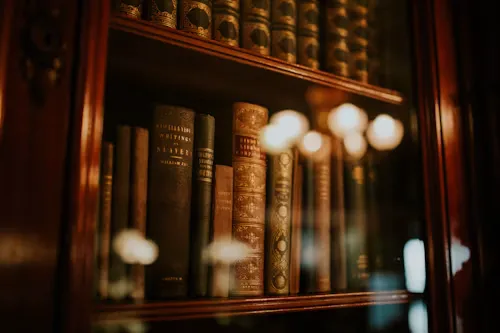 A close-up of antique leather-bound books inside a wooden glass-front cabinet with reflections of chandelier lights.