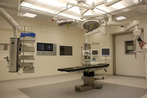 Modern hospital operating room with surgical table, overhead lights, and medical monitors.