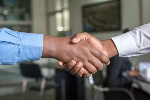 Two individuals in blue and white shirts shaking hands in an office setting.