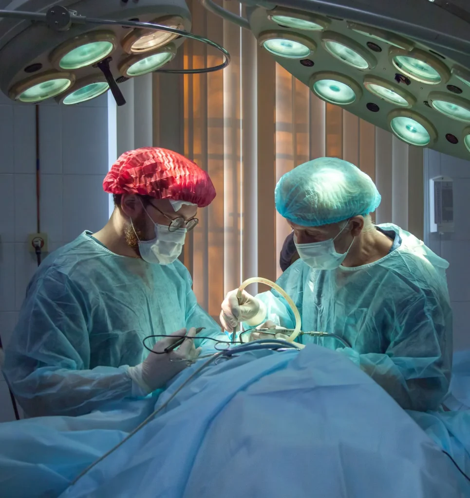 Two surgeons wearing surgical masks and caps performing surgery under overhead operating lights.