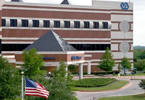 Exterior view of a brick and beige VA medical center building with American flag and landscaping.
